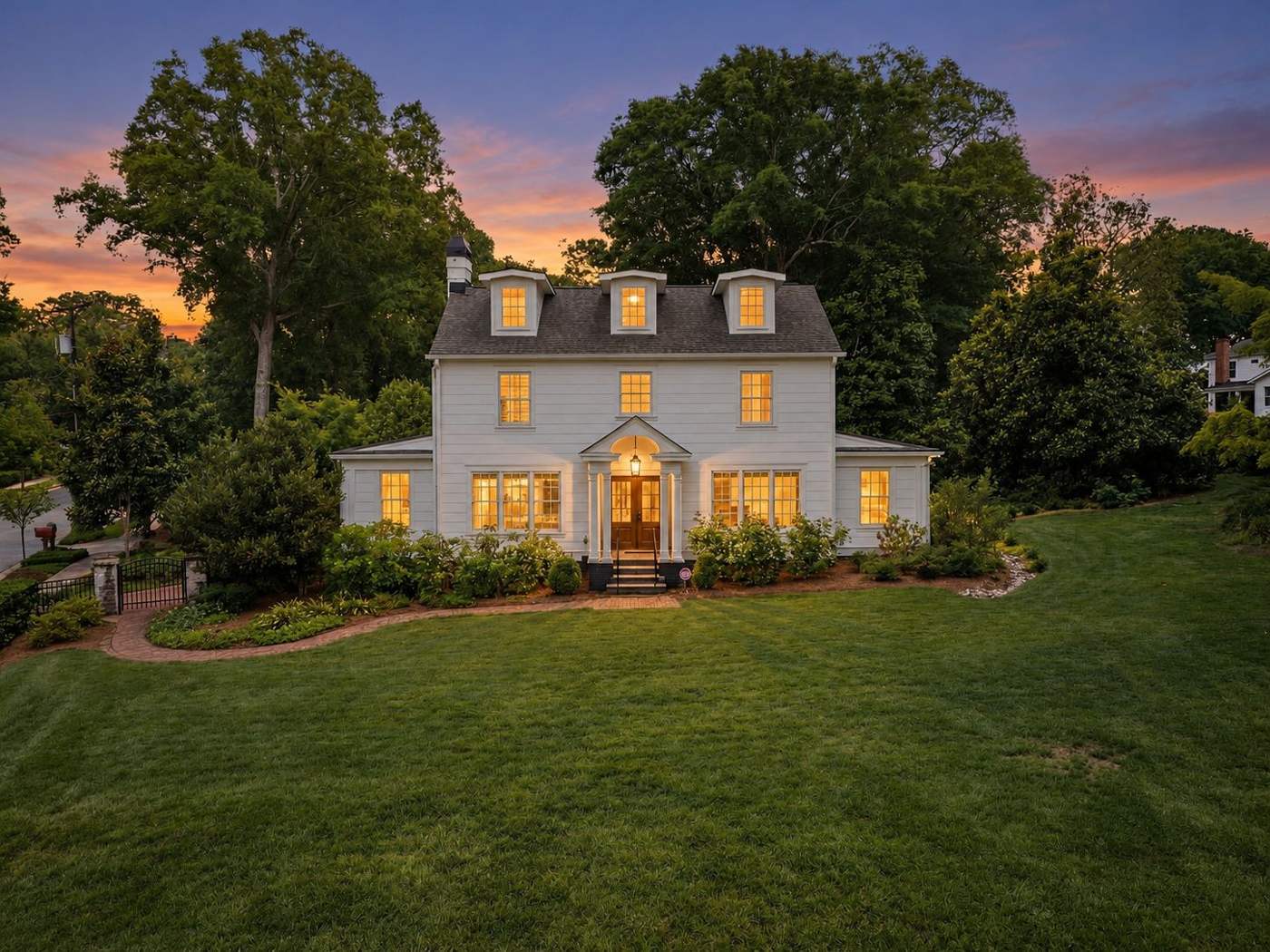 The front of 225 West Faris Road at dusk, a white colonial with dormers and lit windows behind a curved lawn